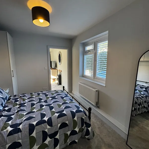 Bedroom window with shutters and a radiator beneath it, and the door through to the living room