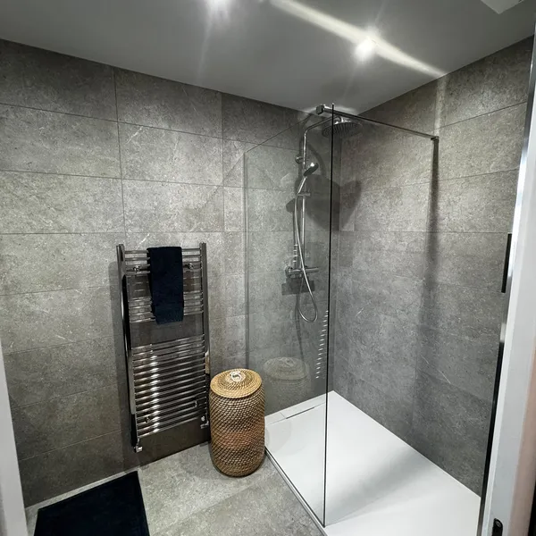 Wet room tiled floor to ceiling in grey, with a heated towel rail beside the zero-step shower