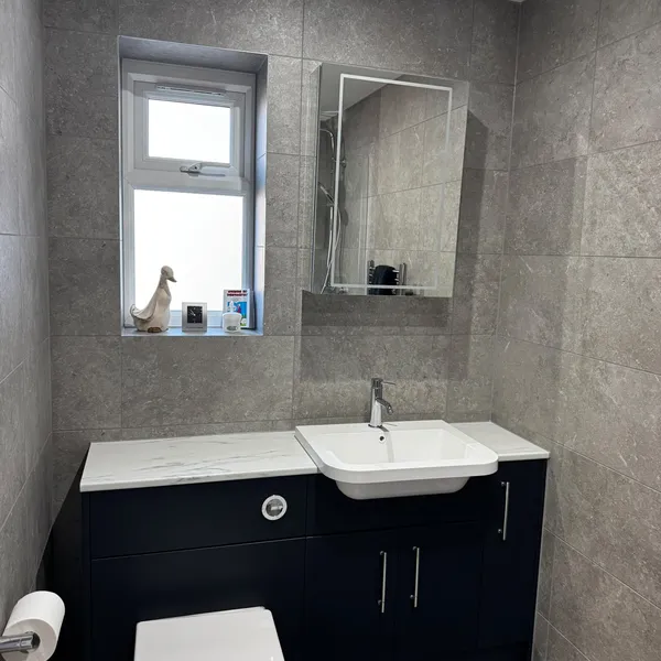 Navy vanity unit with an inset basin and a WC with a concealed cistern, under a window and an illuminated mirror cabinet