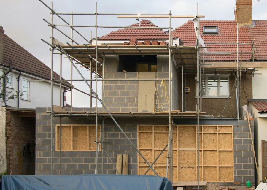 Semi-detached house under scaffolding, with a rooflight in its red-tiled roof and a new blockwork extension going up at the back