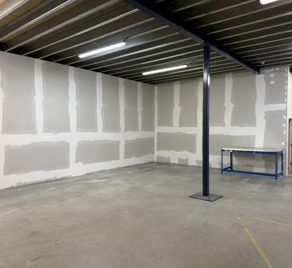 Taped and jointed plasterboard walls around a steel column, with a workbench along the far wall