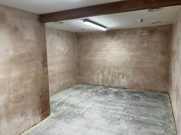 A room with its walls freshly plastered, under a boxed beam and a strip light
