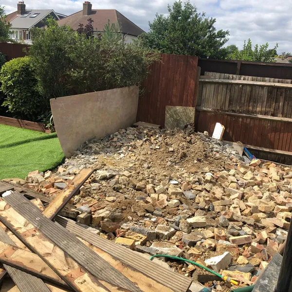 Back garden before the build, with a pile of brick rubble and old decking boards against the fence