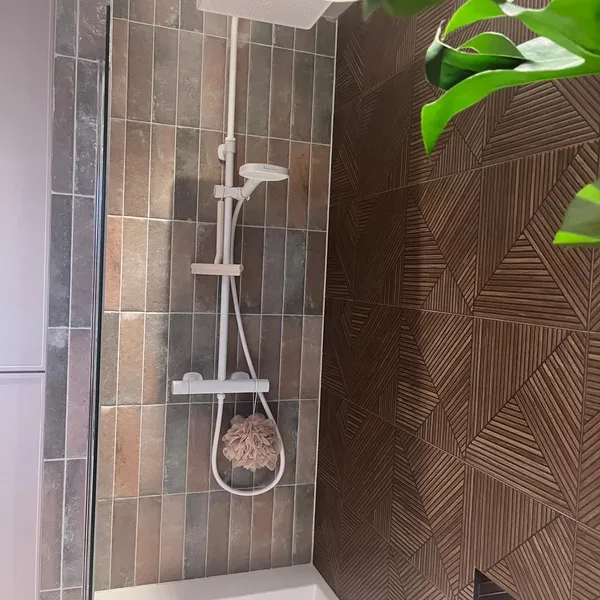 Shower over the bath, with a white thermostatic shower and a mix of glazed and textured tiles