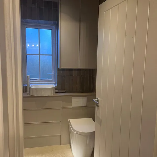 Family bathroom seen through the door, with a back-to-wall WC set into the vanity run and a tall cupboard above