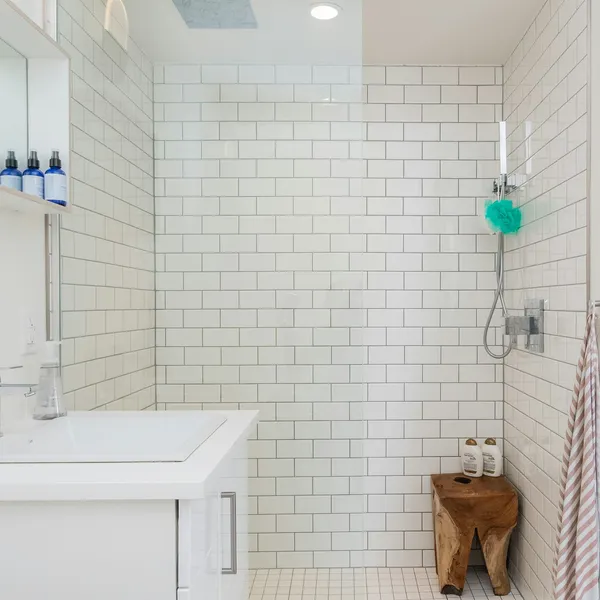 Shower room lined with white metro tiles, with a wooden stool beside the enclosure