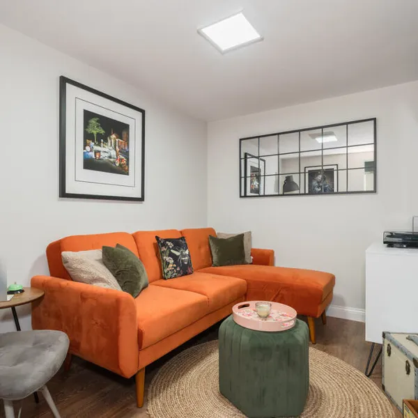 TV room in the converted garage, with an orange corner sofa, a wall-mounted television, a window-style mirror and a wood-effect floor