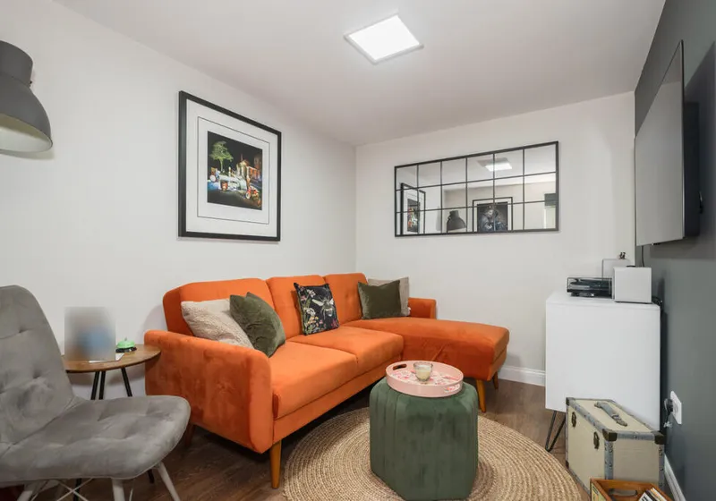 TV room in a converted garage in Horsham, with an orange corner sofa, a wall-mounted television and a wood-effect floor