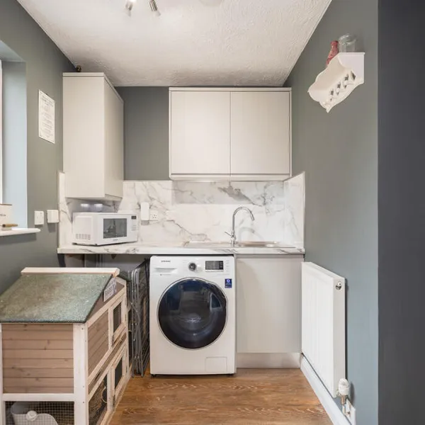 Utility section at the back of the converted garage, with pale grey units, a marble-effect worktop and splashback, a sink and a washing machine