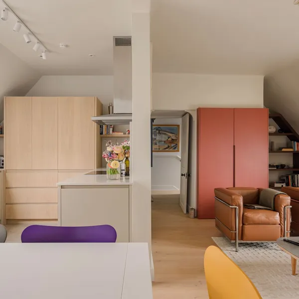 Oak kitchen opening into a living room, with a full-height red built-in cupboard and shelving fitted into the eaves