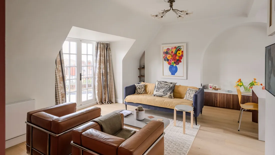 Living room of a top-floor flat we refitted, with leather armchairs, built-in shelving and French windows under the eaves