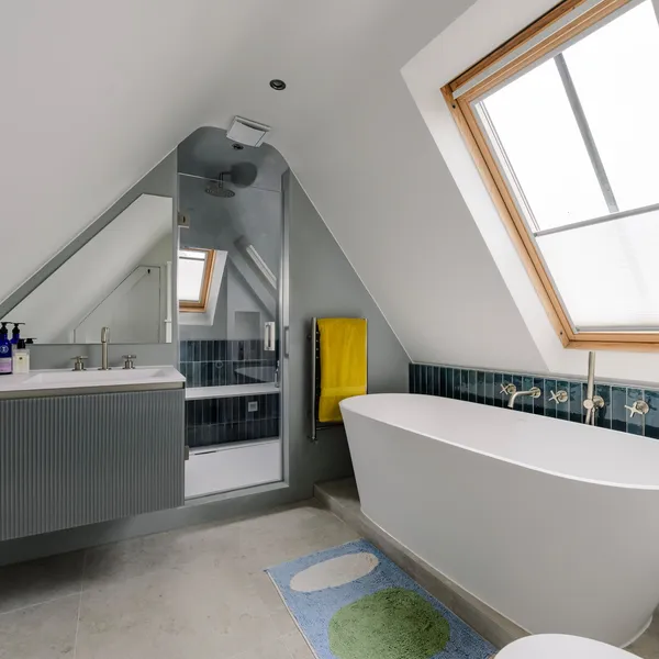Loft bathroom with a freestanding bath under a roof window and dark teal tiles behind it
