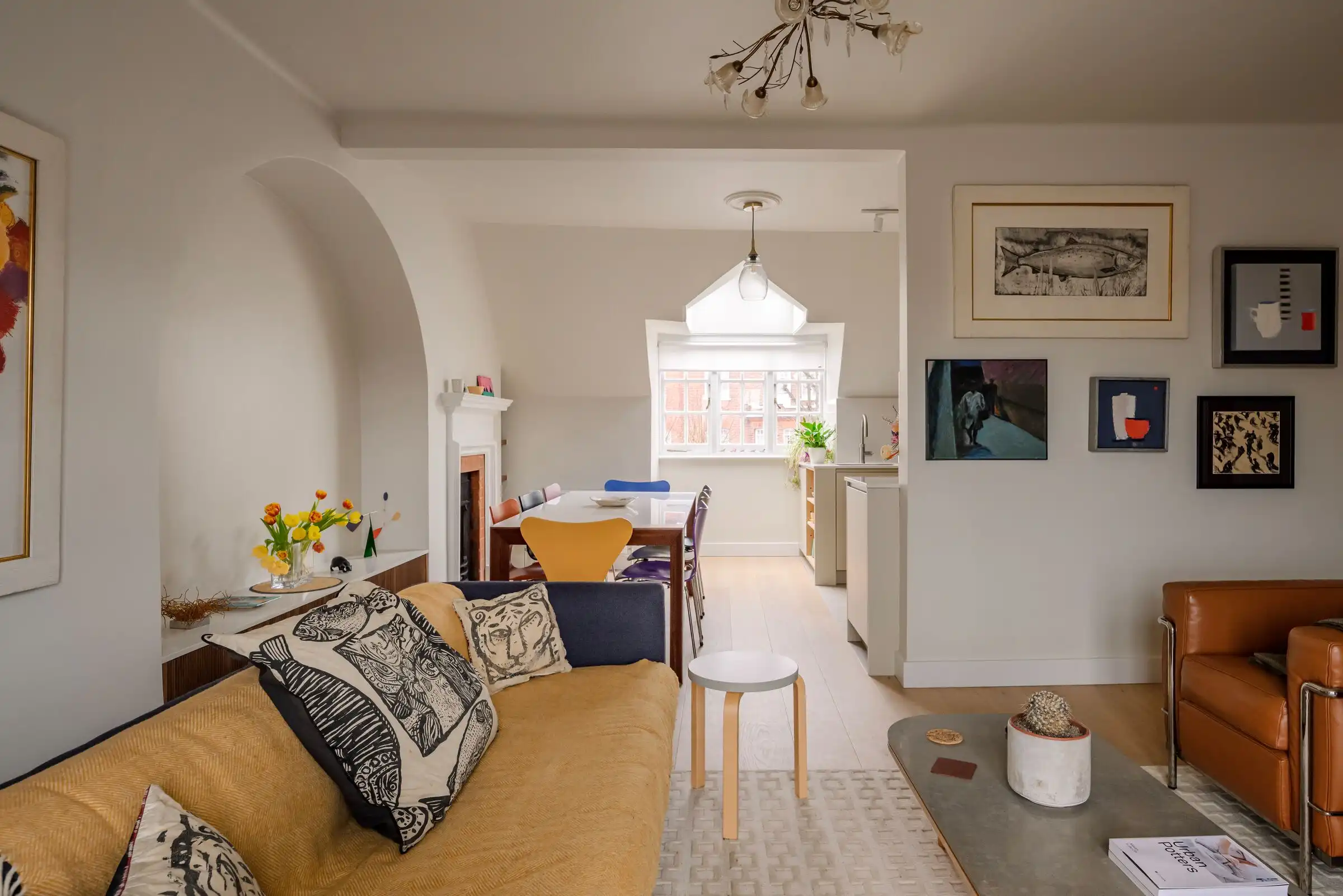 Open-plan loft living room with a mustard sofa and leather armchairs, looking through to the dining table, an arched alcove and the window beyond