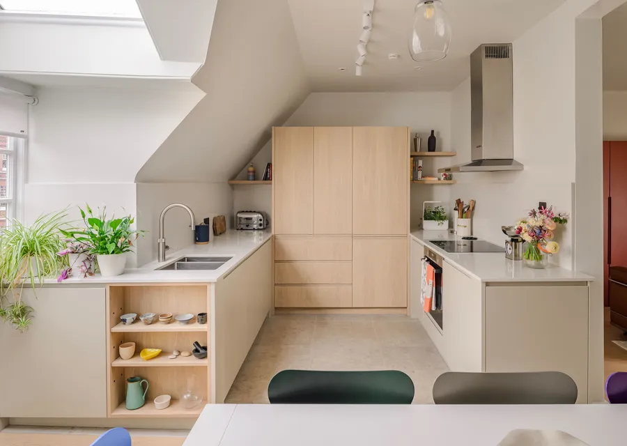Pale oak kitchen fitted under a sloping loft ceiling, with a full-height tower of handleless units, a stainless steel extractor and open shelves at the end of the run