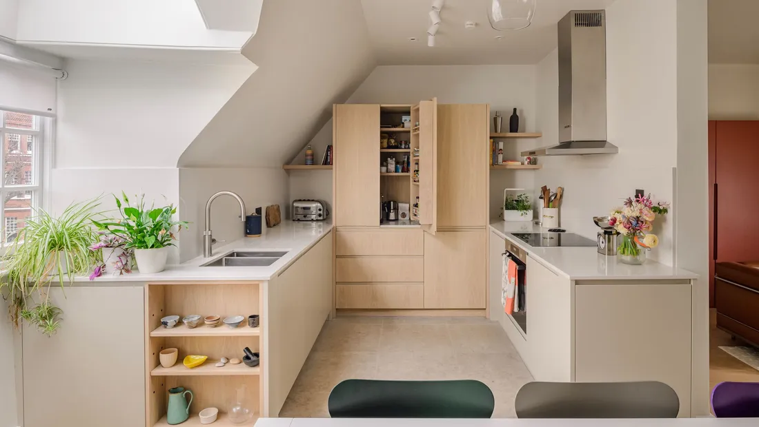 Oak kitchen fitted under a sloping loft ceiling, with the larder cupboard open beside the hob