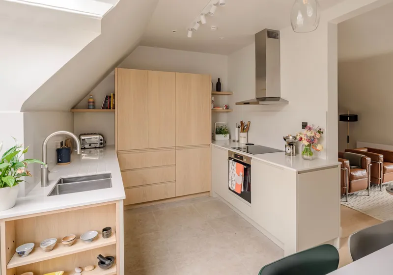Oak kitchen with a full-height tower of handleless units beside the hob run, under a sloping ceiling