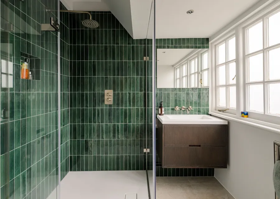 Shower room lined floor to ceiling in green glazed tiles, with a frameless glass screen, a recessed niche and a dark wood vanity under the window