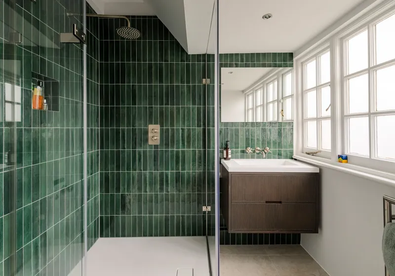 Shower room lined in green glazed tiles, with a frameless glass screen and a dark wood vanity