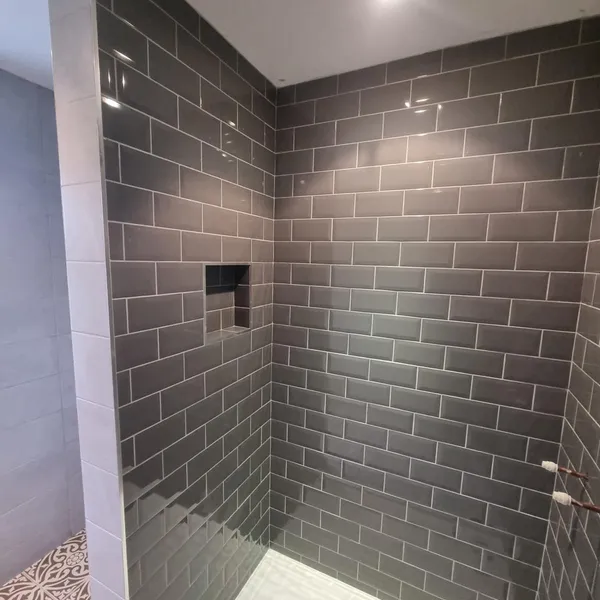 Walk-in shower lined in grey metro tile, with a recessed niche in the back wall