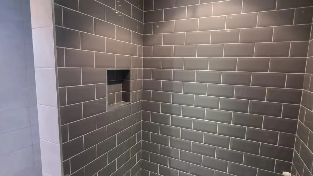 Walk-in shower lined in grey metro tile, with a recessed niche in the back wall