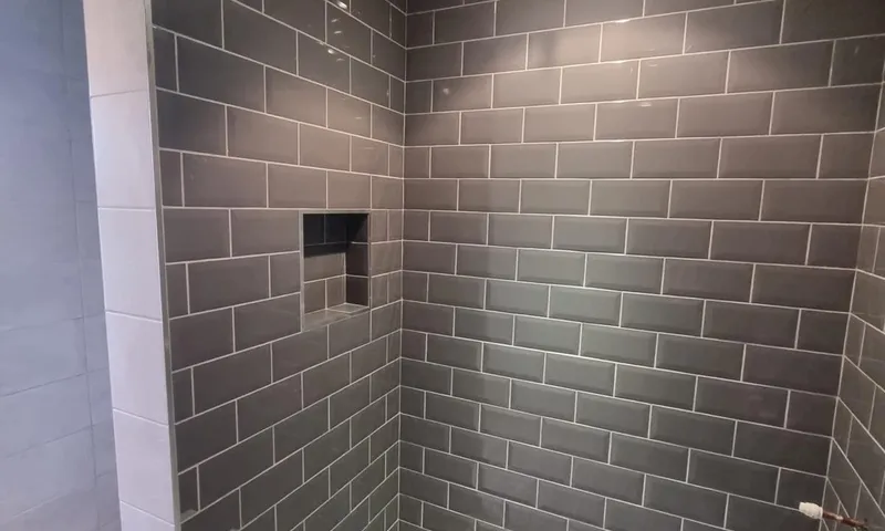 Walk-in shower lined in grey metro tile, with a recessed niche in the back wall